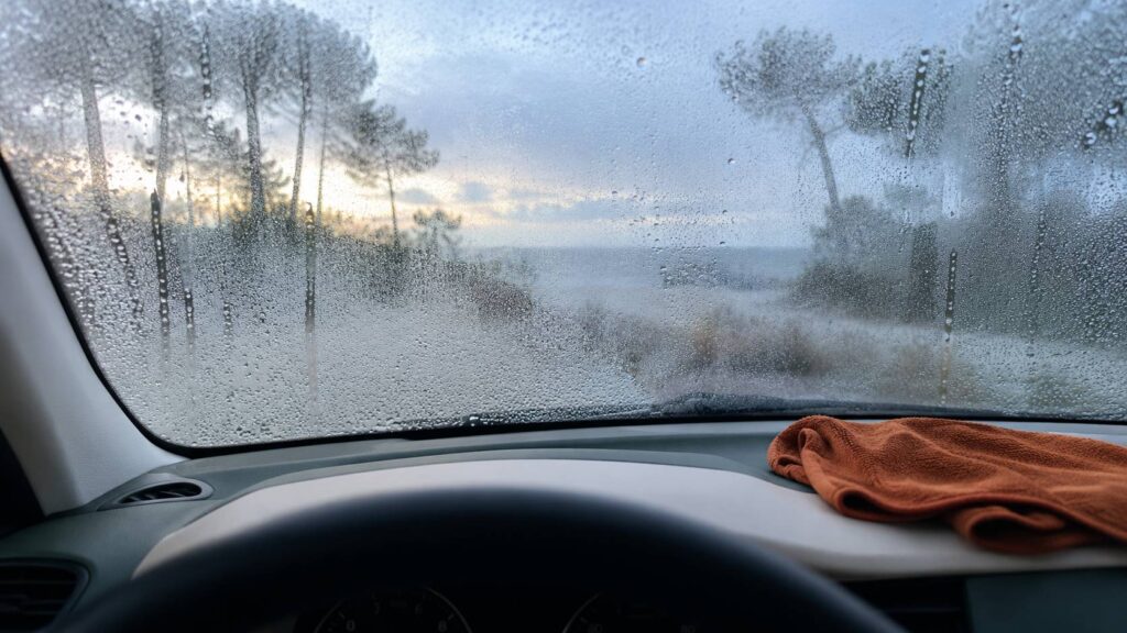 Pare-brise embué vu de l'intérieur d'une voiture au petit matin avec un chiffon sur le tableau de bord
